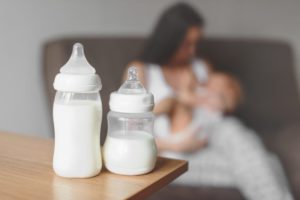 Milk bottles and a mother breastfeeding her baby