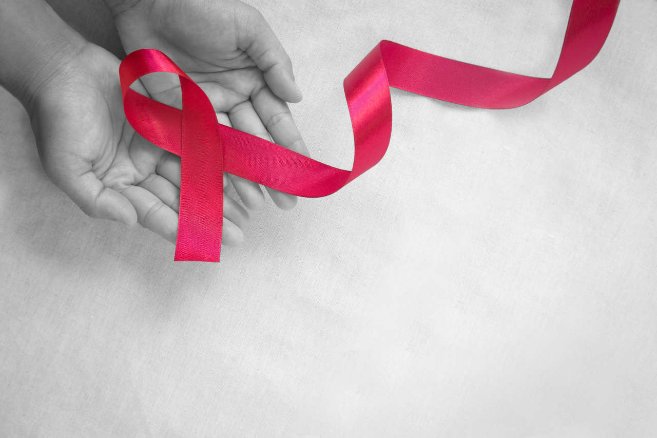 Hands holding Red burgundy ribbon bow on white fabric background with copy space, symbol of Multiple Myeloma awareness.