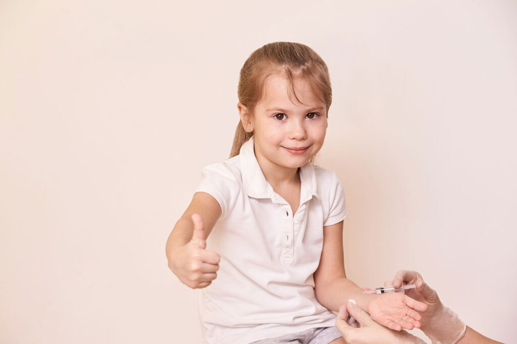 A young girl holding up her thumb while receiving an infusion
