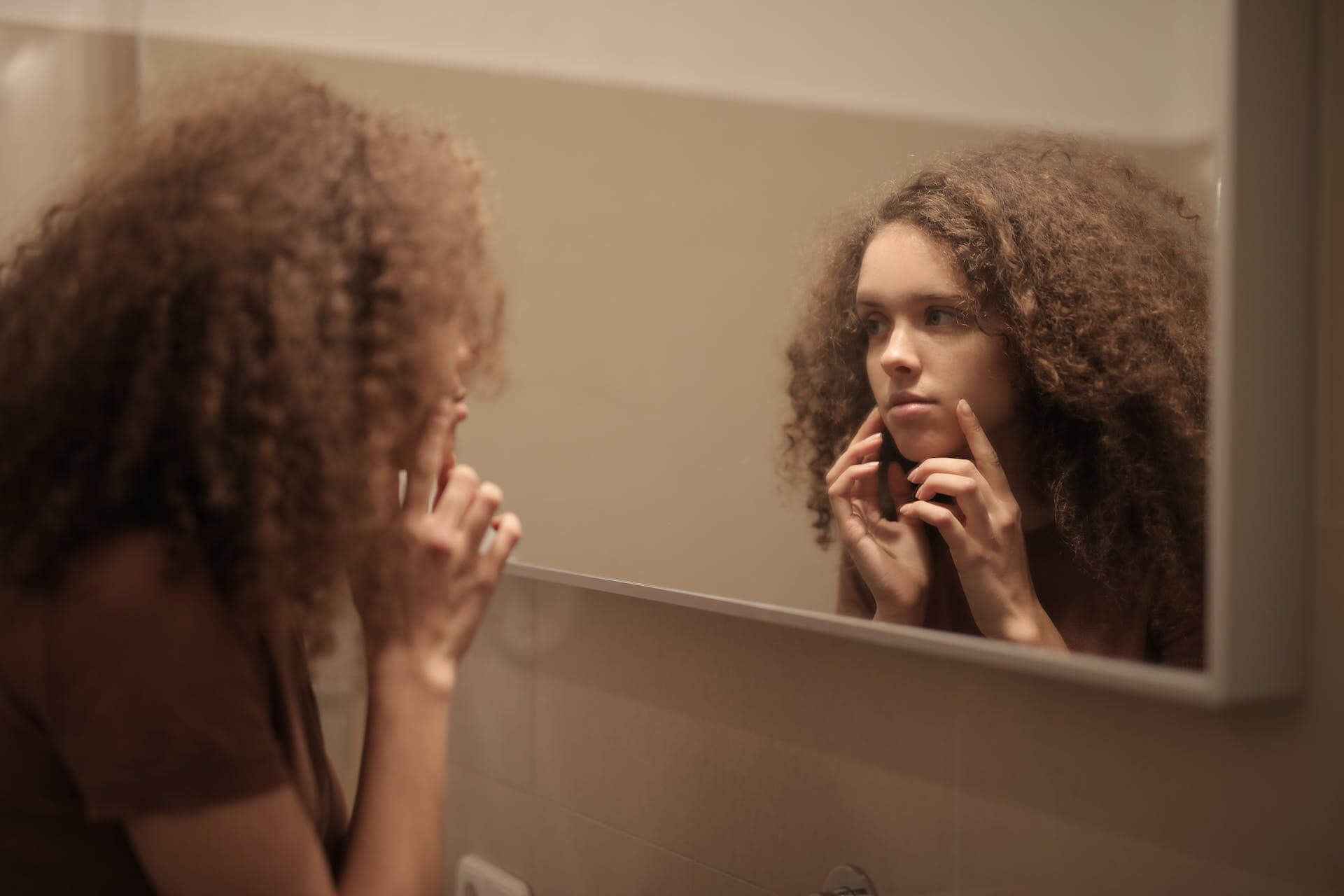 Young woman looking at her skin in the mirror