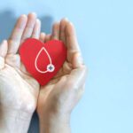 Hemophilia patient's hands holding red heart and blood drop