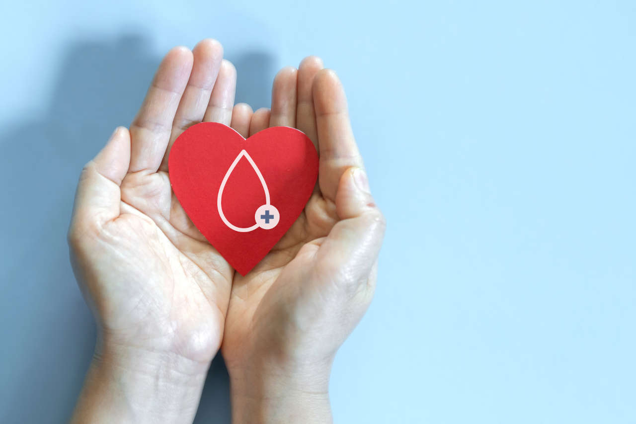 Hemophilia patient's hands holding red heart and blood drop