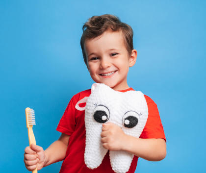 A smiling boy holding a plush tooth and a toothbrush.