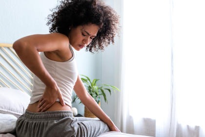 A woman in bed holding her lower back in pain