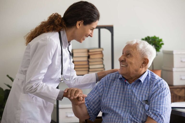 A nurse holding an old man’s hand and smiling