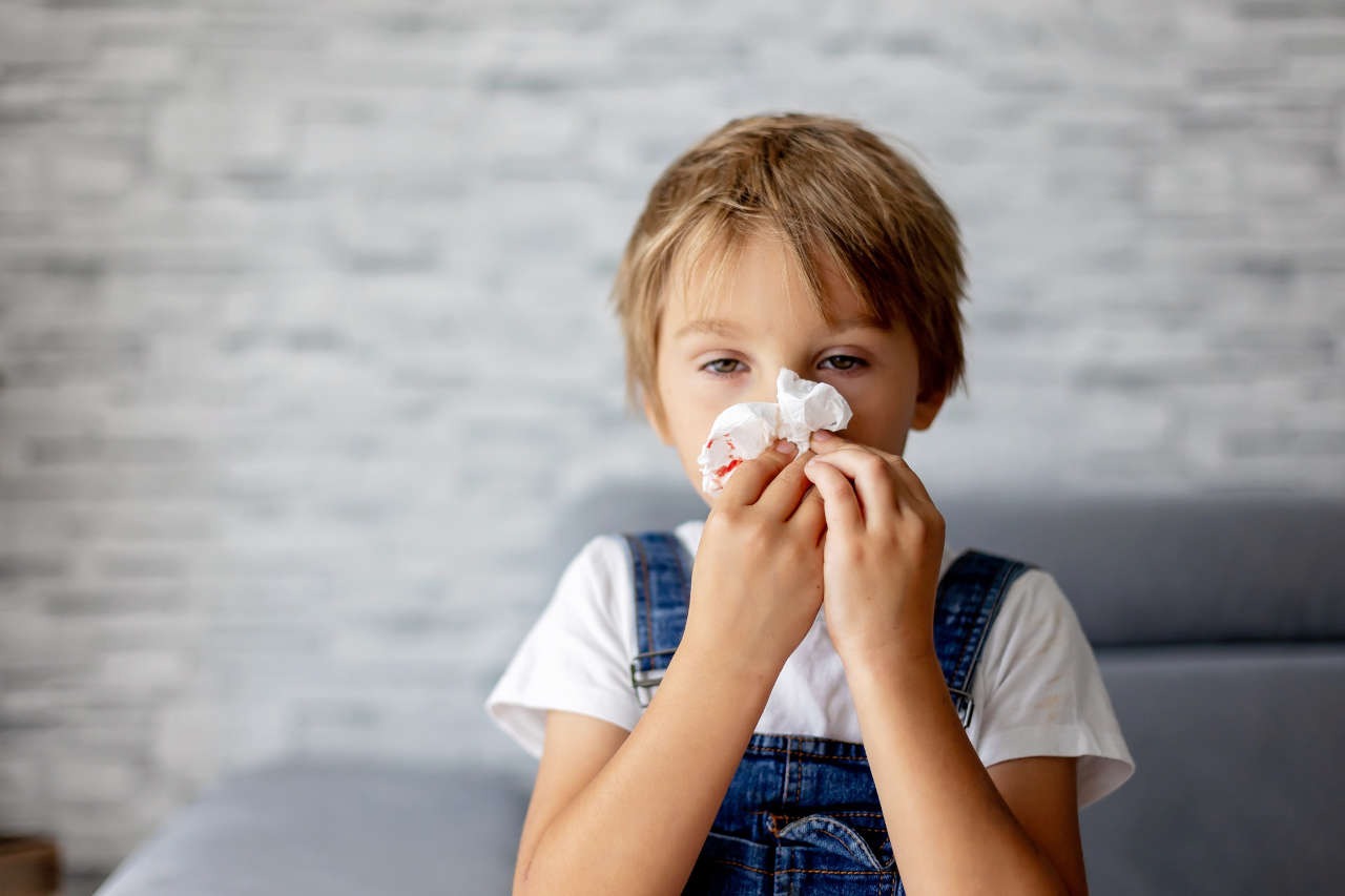 A sick child holding a tissue in front of his bleeding nose