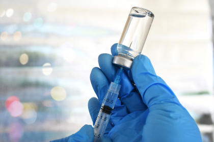 Gloved hands holding syringe and withdrawing vaccine from a vial