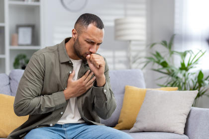 Man on couch coughing and experiencing side effects of Benefix