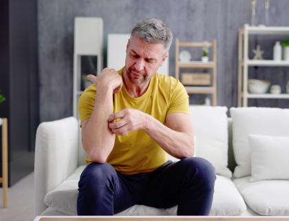Man on couch scratching an itch on his arm. Itching is one of the side effects of Esperoct.