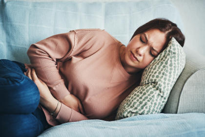 Woman on couch holding stomach due to pain caused by side effects of taking Ixifi