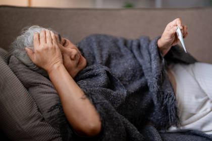 Woman with a fever lying on couch, suffering a side effect from taking Neupogen